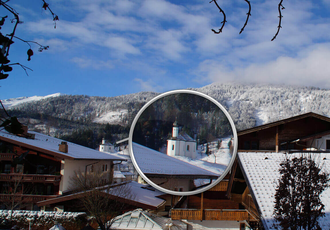 Kamera-Zoom: Ein verschneites Dach und eine Kirche werden herangezoomt.