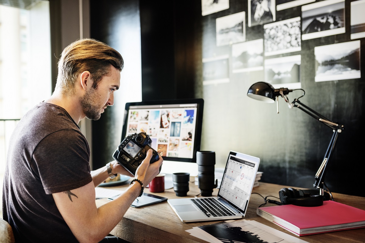 Junger Mann sitzt an seinem Schreibtisch und verwaltet seine digitalen Fotos