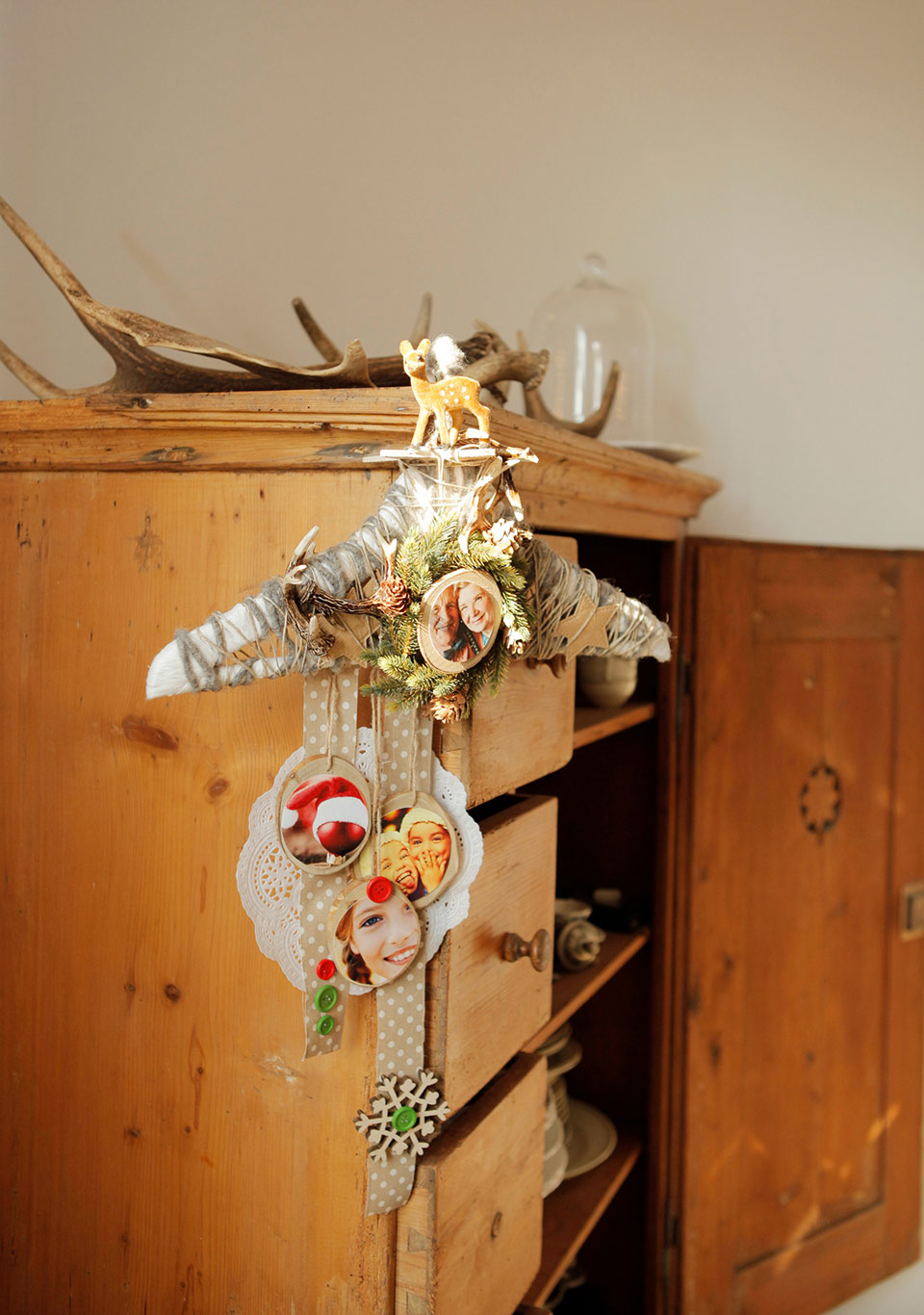 Ein Kleiderbügel, verziert mit weihnachtlicher Dekoration und Fotos, hängt an einem Schrank