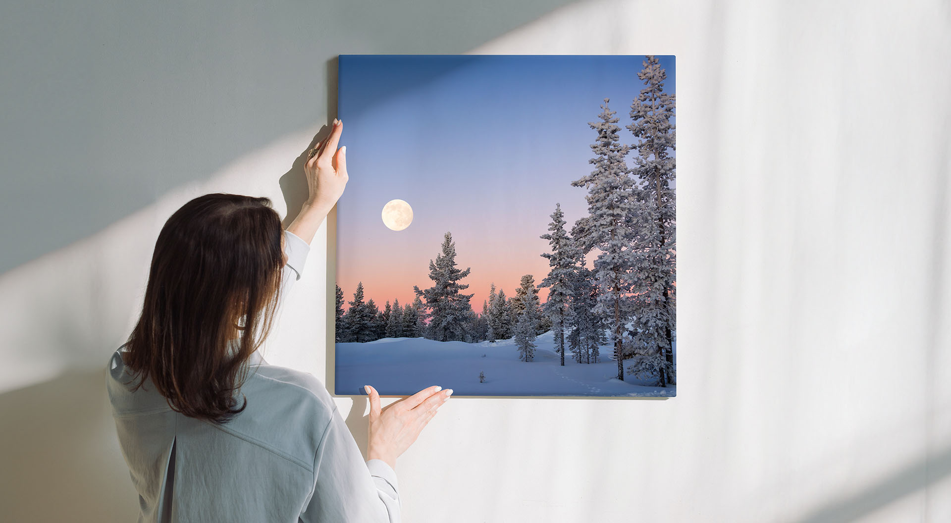 En kvinna som hänger en målarduk med ett vinterlandskap på väggen