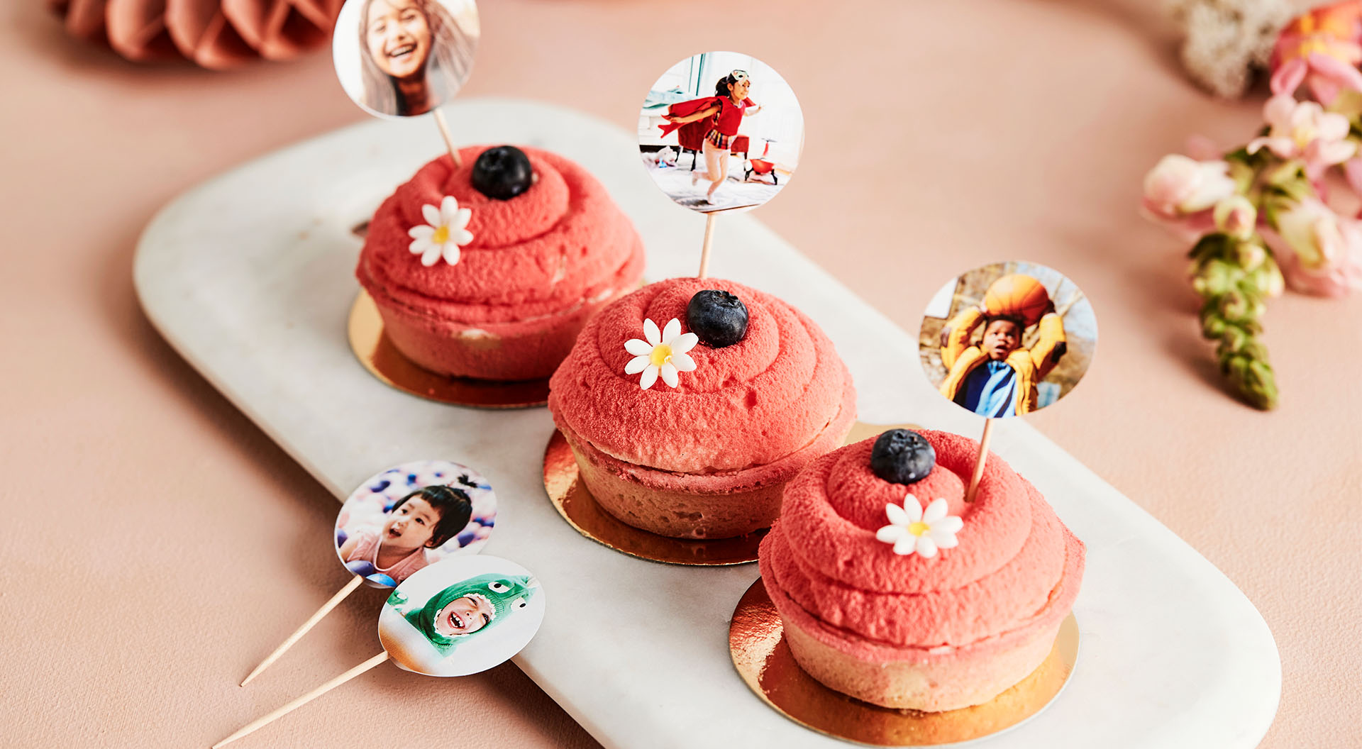 Cupcakes werden mit Deko-Stäbchen verziert, auf denen Bilder des Geburtstagskindes und der Gäste zu sehen sind.